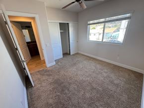 San Diego apartment for rent - A room with a carpeted floor and a window showing a view of a pool and houses outside.