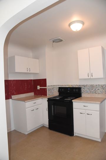 Trinidad house for rent - an empty kitchen with white cabinets and a black stove