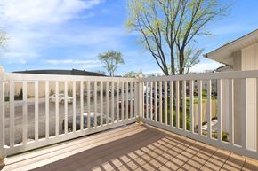Geneva apartment for rent - A white fence encloses a patio with a view of a parking lot and trees.