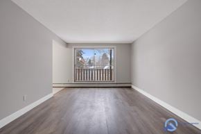 Edmonton apartment for rent - A spacious room with wooden floors and a large window overlooking a balcony.