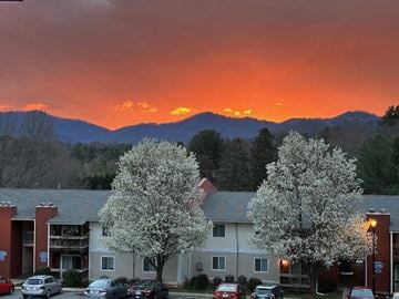 Asheville apartment for rent - A sunset view of a mountain range with a building and trees in the foreground.
