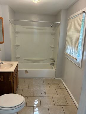 Mobile house for rent - A white toilet is in a bathroom with a white tub and a window with blinds.