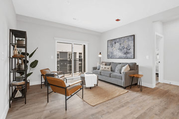 St. Louis apartment for rent - A living room with a grey couch, a brown chair, and a large painting on the wall.