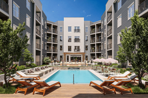 St. Louis apartment for rent - A large swimming pool surrounded by wooden deck chairs and lounge umbrellas in front of a modern apartment complex.
