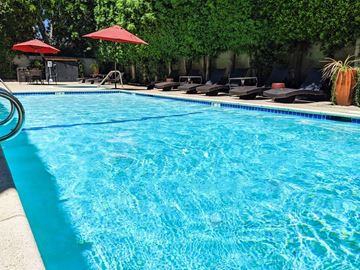 Van Nuys apartment for rent - A swimming pool with red umbrellas and lounge chairs.