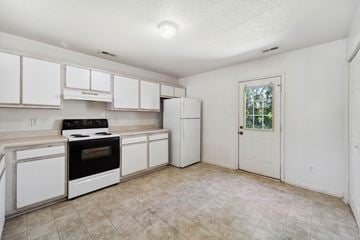 Jacksonville house for rent - A kitchen with white cabinets and appliances, a window, and a door.