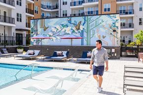 Durham apartment for rent - A man is walking in a pool area with a mural of a tree and birds on the wall.