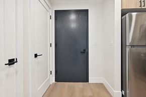 Jersey City apartment for rent - a black door in a room with white walls and a refrigerator