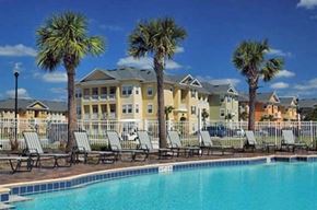 Kissimmee apartment for rent - a large pool with chairs and palm trees in front of a building