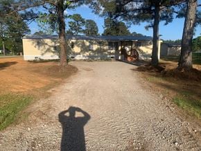 Greenwood house for rent - A shadow of a person is cast on a gravel path leading to a building.