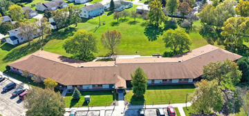 Seymour triplex for rent - A large building with a brown roof is surrounded by a grassy area and trees.