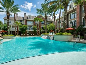 Houston apartment for rent - A swimming pool surrounded by palm trees and buildings.