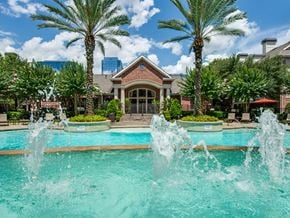 Houston apartment for rent - A pool with water fountains in front of a building with a red roof.