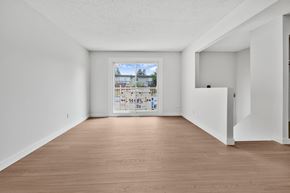 Calgary apartment for rent - A room with wooden floors and white walls, with a large window that shows a view of a street with cars and buildings.