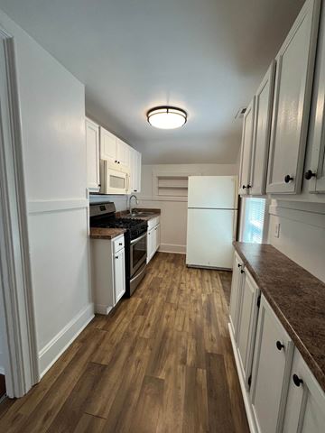 Waukegan apartment for rent - a kitchen with white cabinets and white appliances and wood floors