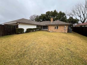 Richardson house for rent - A house with a brown roof and a white wall is surrounded by a grassy yard.
