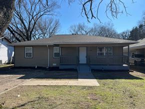 Dallas house for rent - A house with a gray roof and a white door is surrounded by a grassy area.