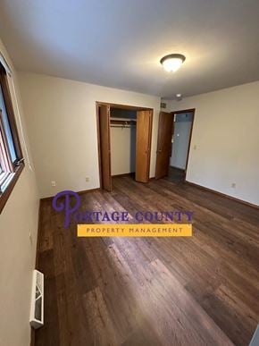 Stevens Point apartment for rent - A room with wooden floors and a Portage County Property Management logo.