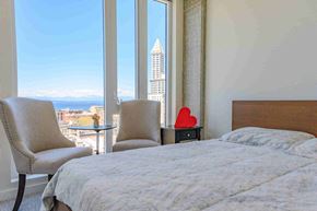 Seattle apartment for rent - A bedroom with a large bed, a chair, and a view of a cityscape through a window.