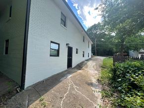 Atlanta apartment for rent - A white building with a black door and windows is surrounded by greenery.