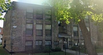 Chicago apartment for rent - A brick building with a black fence and a tree in front.