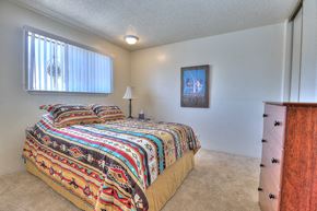 Albuquerque apartment for rent - A bedroom with a bed covered in a multicolored comforter and a painting on the wall.