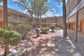 Albuquerque apartment for rent - A courtyard with a bench and trees in front of apartment buildings.