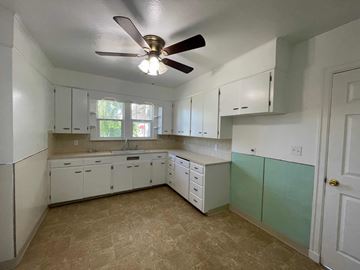 Kelso house for rent - an empty kitchen with white cabinets and a ceiling fan