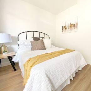 Vancouver apartment for rent - A bed with a white comforter and a yellow throw blanket.