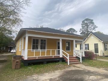 Mobile house for rent - A yellow house with a white porch and a brown trash can in front of it.