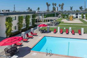 Santa Fe Springs apartment for rent - A pool with red umbrellas and chairs is surrounded by a fence.