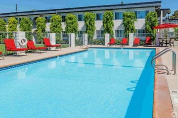 Santa Fe Springs apartment for rent - A swimming pool with red lounge chairs and a building in the background.