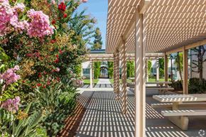 Santa Fe Springs apartment for rent - A walkway with benches and a canopy is surrounded by flowers.