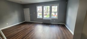 Hillside apartment for rent - A room with wooden floors and a large window.