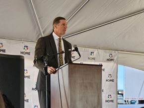Clint apartment for rent - A man in a suit stands at a podium with a microphone, in front of a banner with the word "HOME" on it.