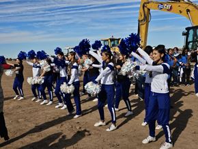 Clint apartment for rent - A group of cheerleaders in blue and white uniforms perform in front of a yellow excavator.