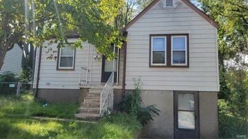 Saint Louis house for rent - A small house with a brown roof and a white door is surrounded by greenery.
