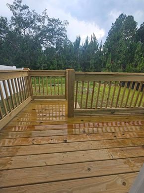 Pensacola house for rent - a deck with wooden railing and grass and trees