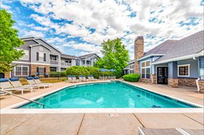 Loveland apartment for rent - A swimming pool in front of a building with a blue sky and clouds in the background.