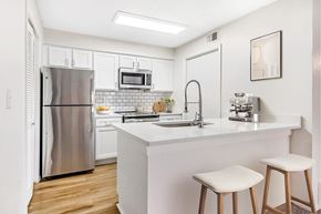 Westminster apartment for rent - A kitchen with a stainless steel refrigerator, a microwave above the stove, a sink with a faucet, and two bar stools.