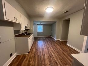 Hattiesburg house for rent - an empty kitchen and living room with wood floors and white cabinets