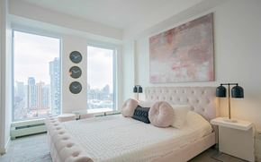 Calgary apartment for rent - A bedroom with a large bed and a city view through the window.