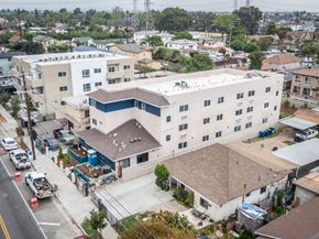 Los Angeles apartment for rent - A large white building with a blue stripe on the side is surrounded by other buildings and vehicles.