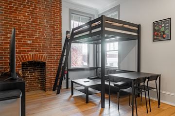Washington apartment for rent - a loft bed in a living room with a red brick fireplace and a dining table
