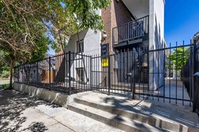 Denver apartment for rent - A black metal fence surrounds a building with a brick wall and a balcony.