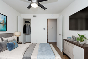 Denver apartment for rent - A bedroom with a bed, a ceiling fan, and a cabinet with a plant on it.