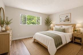 Anaheim apartment for rent - A bedroom with a large bed and a window with a view of greenery outside.