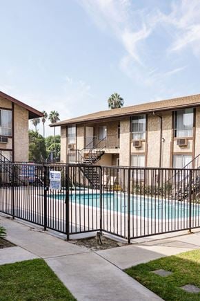 Anaheim apartment for rent - A black fence surrounds a pool in front of a building.