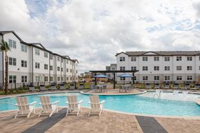 Houston apartment for rent - a swimming pool with chairs and umbrellas in front of apartment buildings