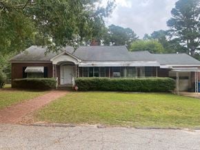 Greenwood house for rent - the front of a brick house with a lawn and trees